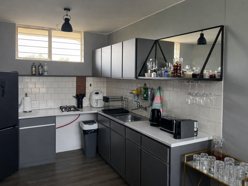 Compact kitchen featuring grey cabinetry, white subway tile backsplash, stainless steel sink, and a built-in gas cooktop with modern industrial-style shelving.