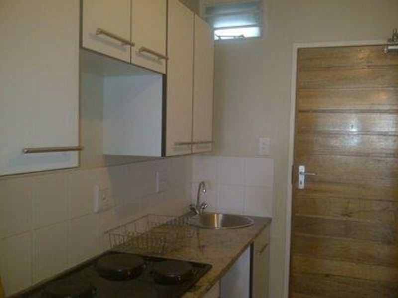 Compact kitchen featuring built-in cabinetry, granite countertops, a stainless steel sink, and an integrated electric hob with tiled splashback.