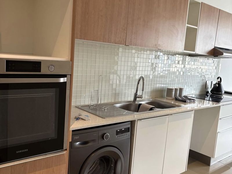 Modern kitchen featuring wood-tone cabinetry, stone countertops, a tiled backsplash, built-in oven, hob, extractor fan, and an integrated washing machine.