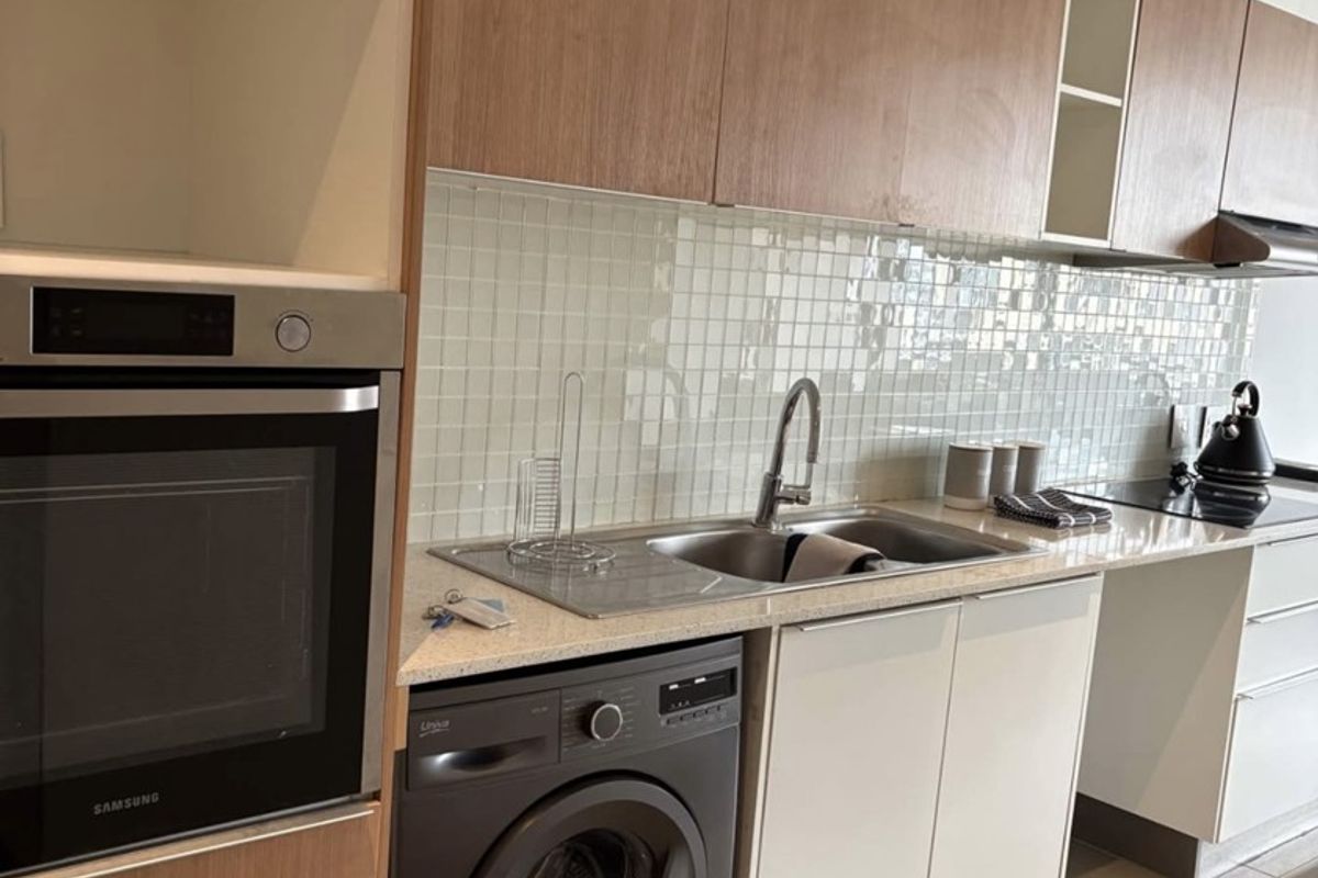 Modern kitchen featuring wood-tone cabinetry, stone countertops, a tiled backsplash, built-in oven, hob, extractor fan, and an integrated washing machine.