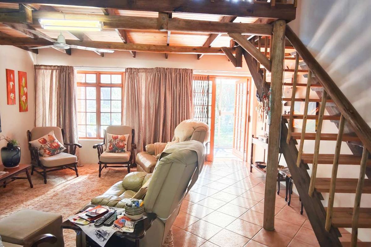 Spacious living area featuring exposed timber ceiling beams, a wooden staircase leading to a mezzanine level, and tiled flooring with direct garden access.