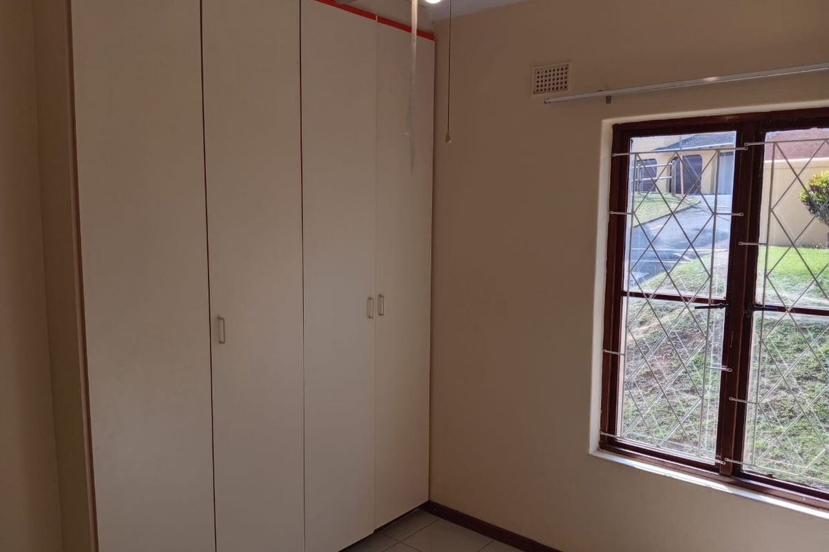 A bedroom featuring built-in cupboards, tiled flooring, and a window with security bars overlooking the exterior.