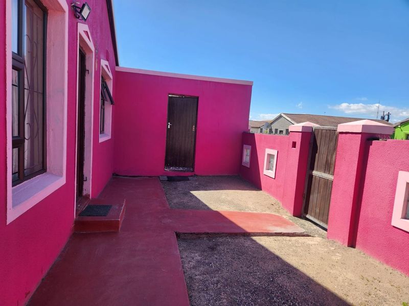 Rear exterior view of the property featuring a painted boundary wall, wooden gate, and a concrete pathway leading to the entrance.