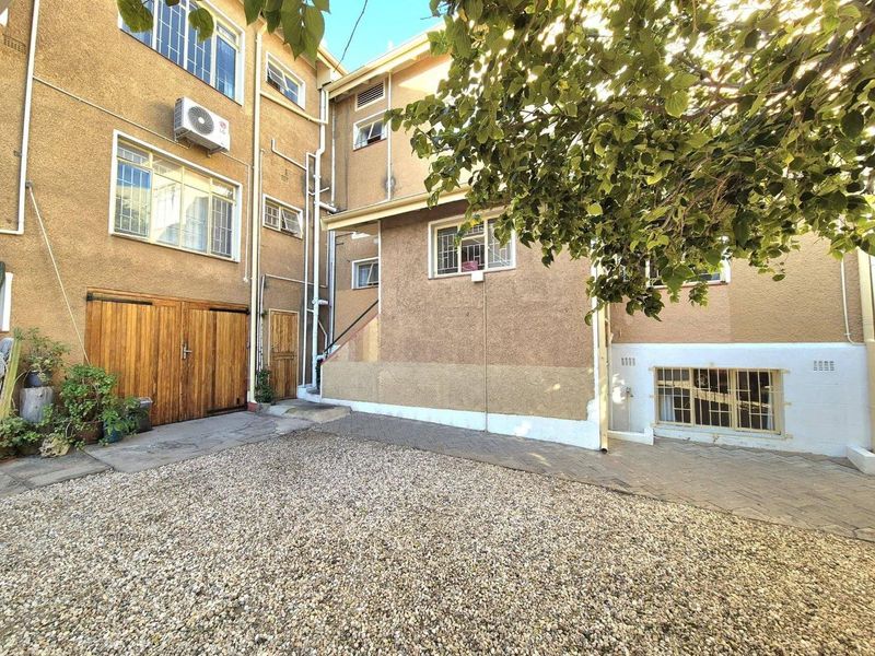 Rear exterior view of the apartment building featuring a gravel courtyard, paved walkway, and integrated garage access with security-fitted windows.
