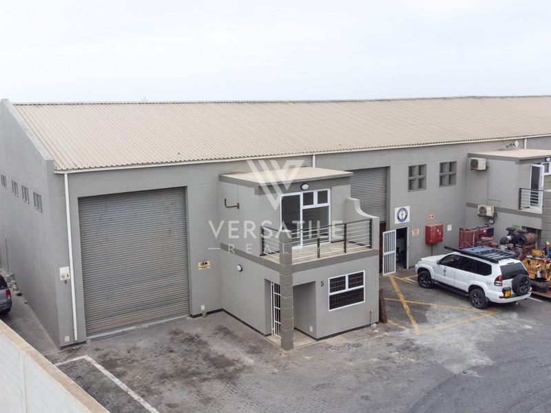 Aerial view of an industrial warehouse unit featuring roller shutter doors, a small balcony, and paved exterior yard space.