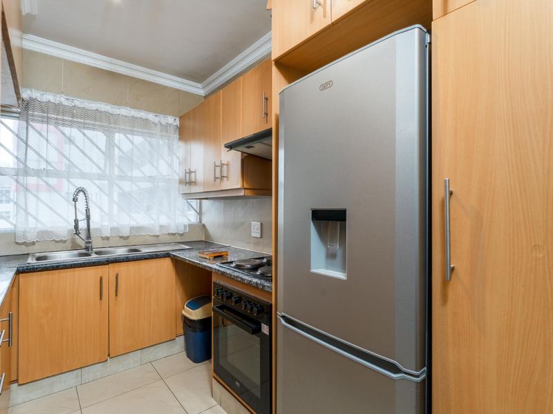 Compact kitchen featuring light wood laminate cabinetry, granite countertops, built-in oven with hob, and a stainless steel double sink with a modern faucet.