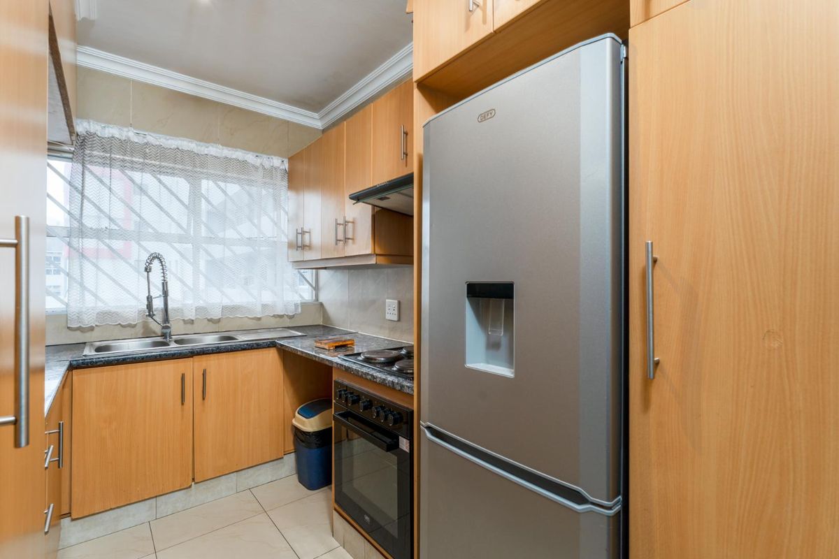 Compact kitchen featuring light wood laminate cabinetry, granite countertops, built-in oven with hob, and a stainless steel double sink with a modern faucet.