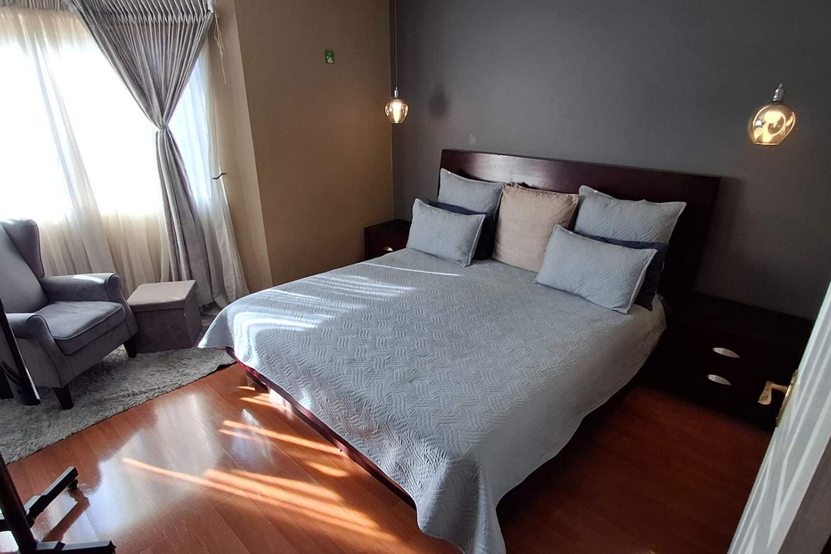 A well-maintained bedroom featuring warm laminate flooring, a built-in headboard, and modern pendant lighting, creating a comfortable and inviting sleeping space.