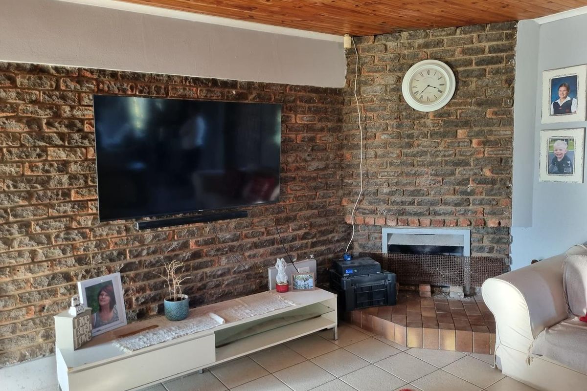 Living room featuring an exposed brick wall, built-in fireplace, tiled flooring, and a timber ceiling.