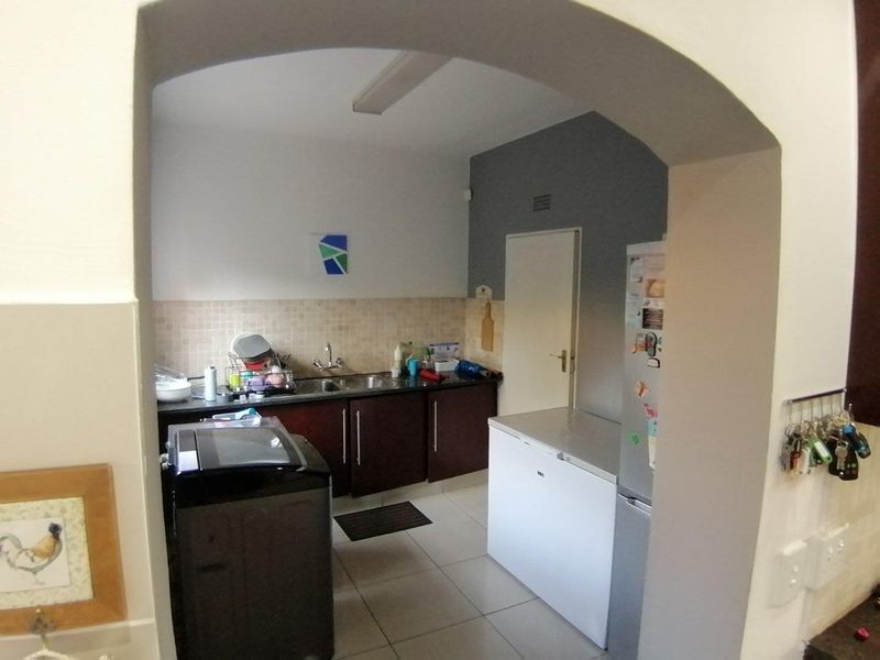 A functional scullery area featuring built-in cabinetry, a double sink, tiled backsplash, and tiled flooring, accessed through a classic arched doorway.