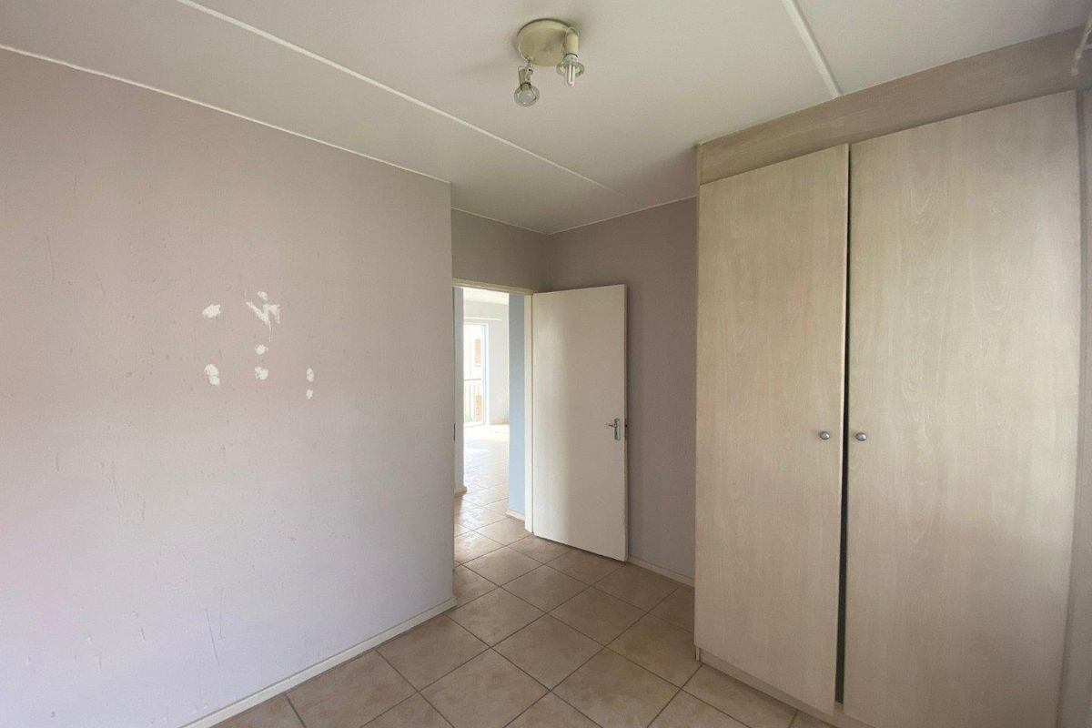 A bedroom featuring built-in wooden cabinetry, tiled flooring, and access to an adjoining room.