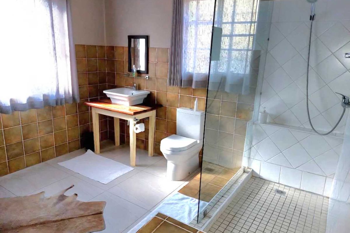 A functional bathroom featuring a glass-enclosed walk-in shower, a vessel sink on a wooden vanity, and a toilet, finished with neutral wall and floor tiling.
