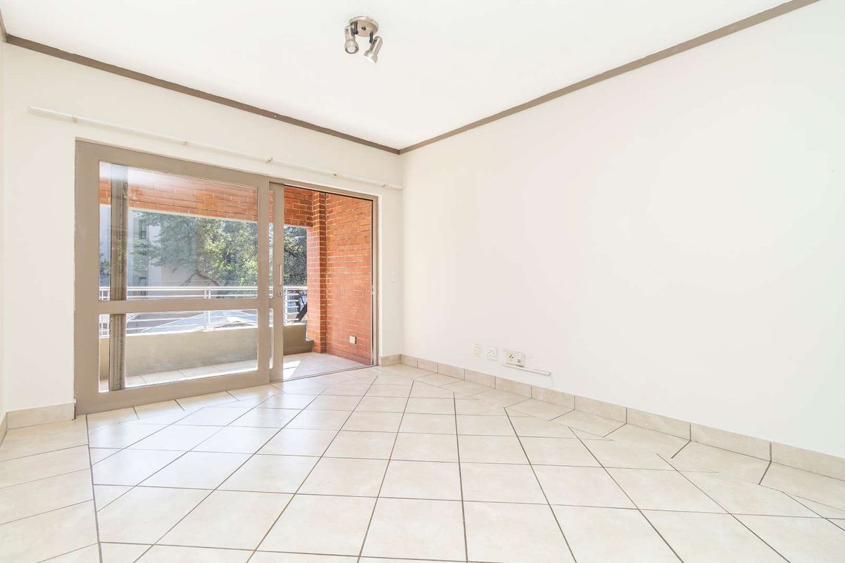 A bright, empty living room featuring neutral tiled flooring and a large sliding glass door providing access to an outdoor balcony area.