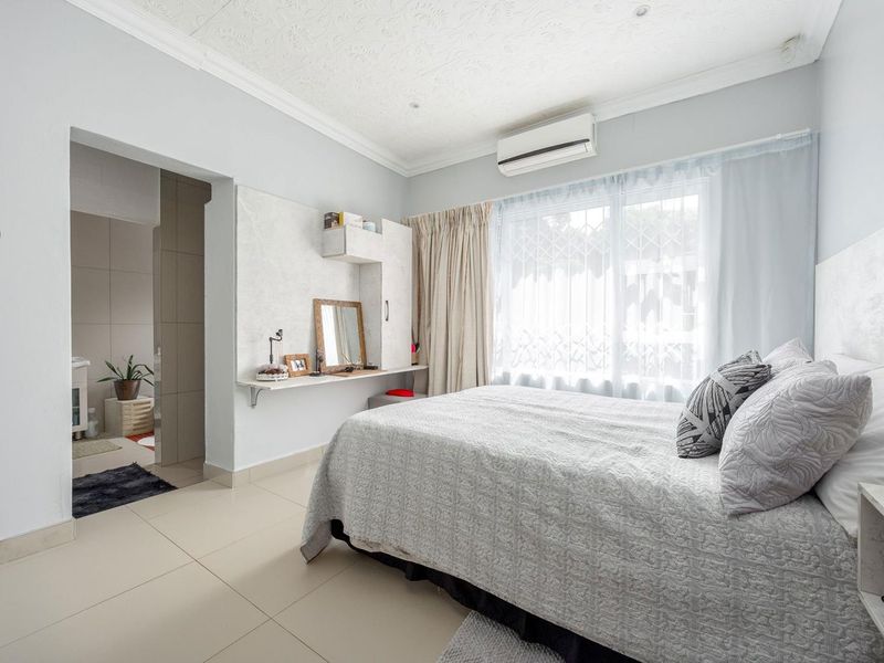 A well-maintained bedroom featuring tiled flooring, a wall-mounted air conditioning unit, and an adjoining en-suite bathroom.