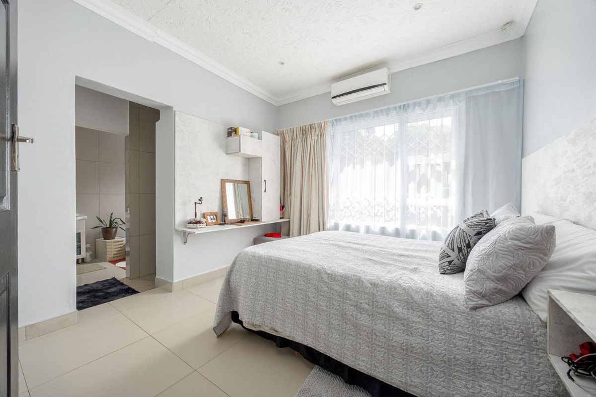 A well-maintained bedroom featuring tiled flooring, a wall-mounted air conditioning unit, and an adjoining en-suite bathroom.