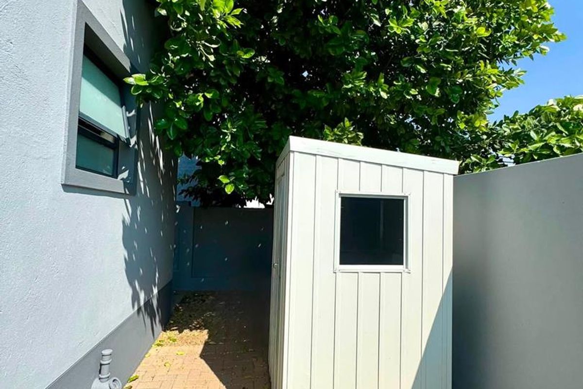 A side or rear exterior area featuring a paved walkway, boundary wall, and a small storage shed structure.