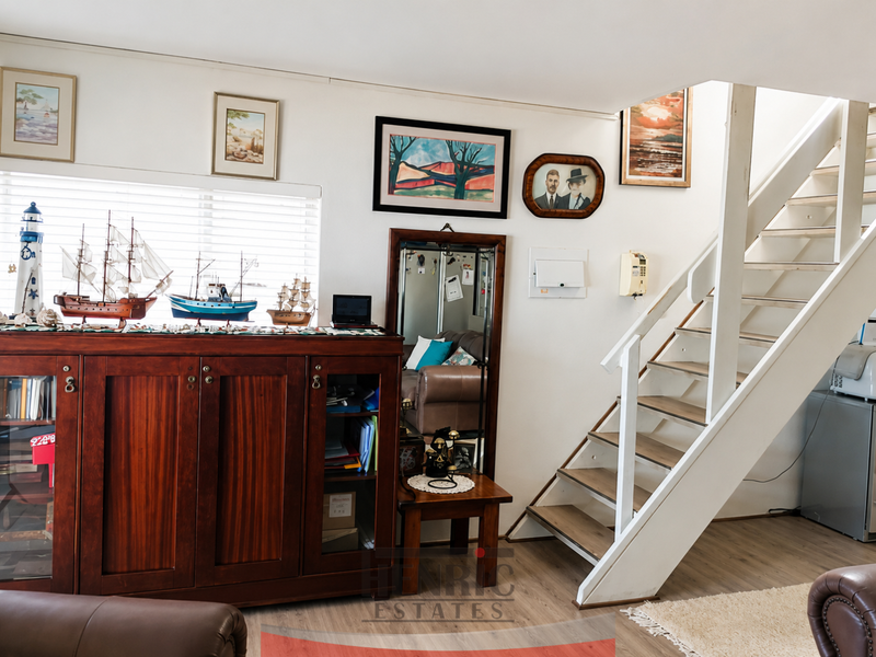 A living area featuring a wooden staircase, venetian blinds, and neutral flooring, providing a functional space with potential for modern updates.