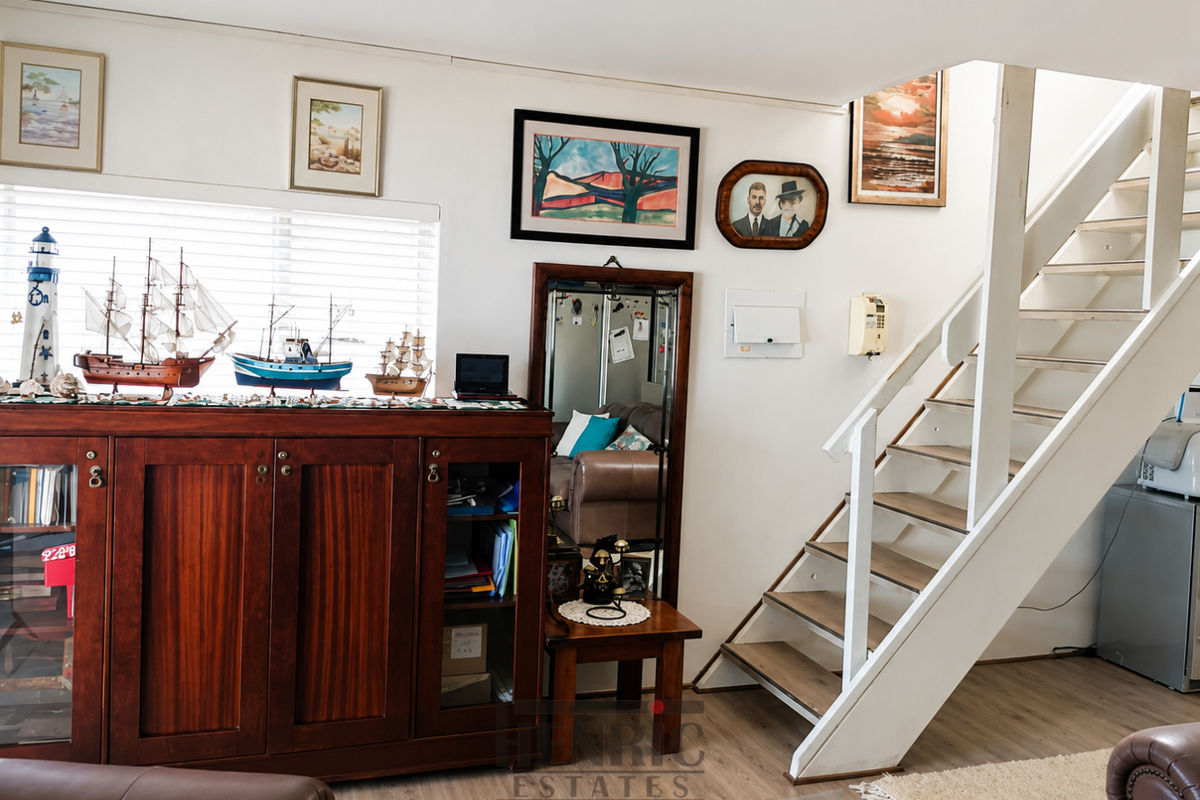 A living area featuring a wooden staircase, venetian blinds, and neutral flooring, providing a functional space with potential for modern updates.