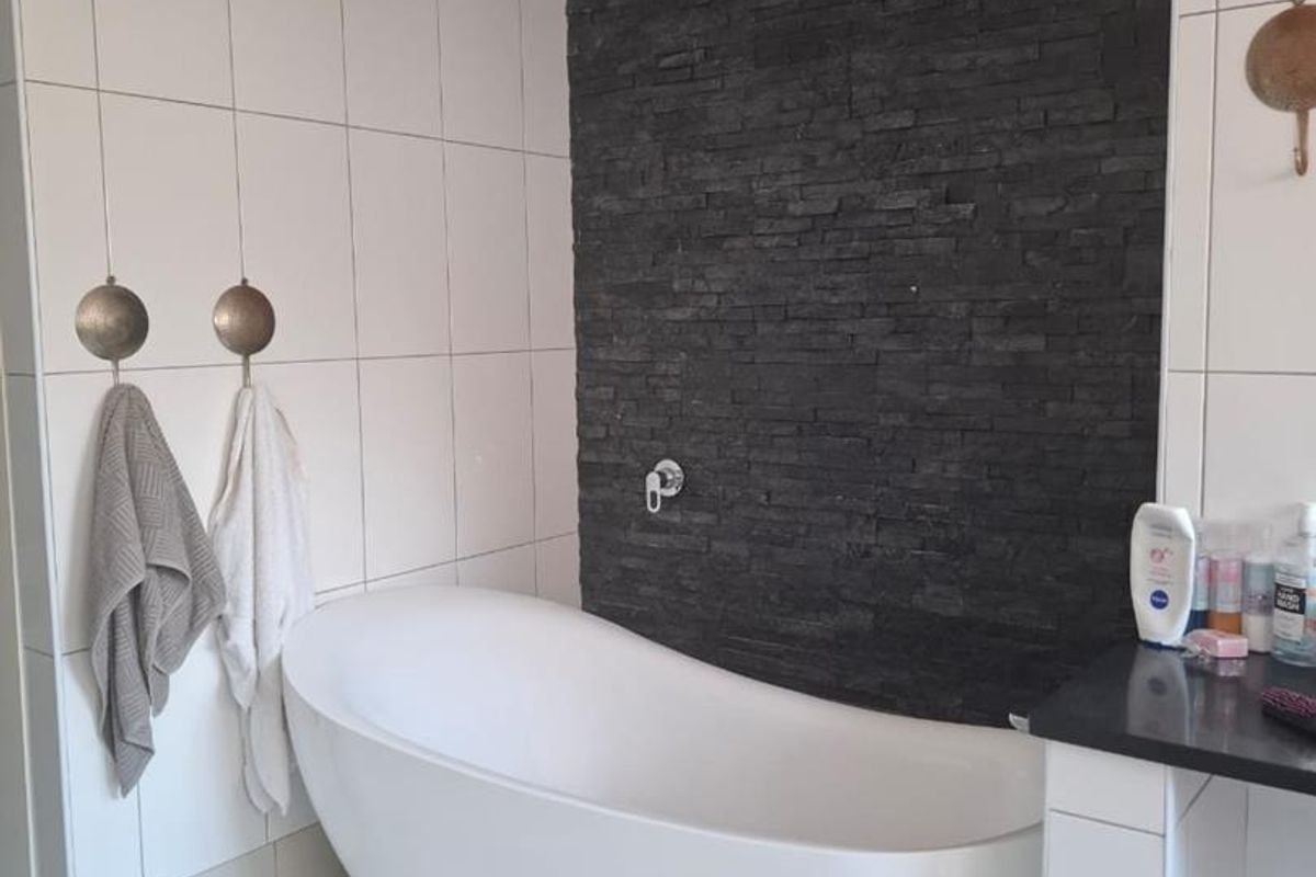 Modern bathroom featuring a freestanding white bathtub set against a striking black stone feature wall with white tiled surrounds.