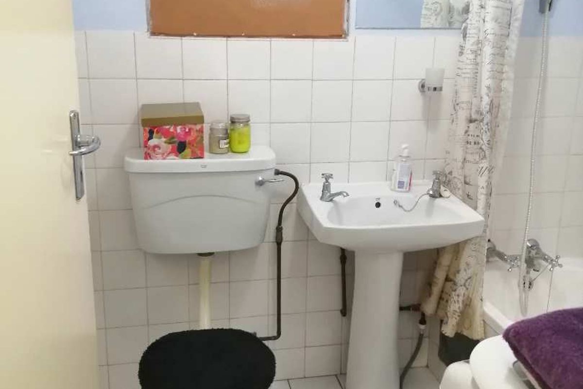 A functional bathroom featuring a pedestal basin, toilet, and bathtub with shower mixer, finished with white wall and floor tiles.
