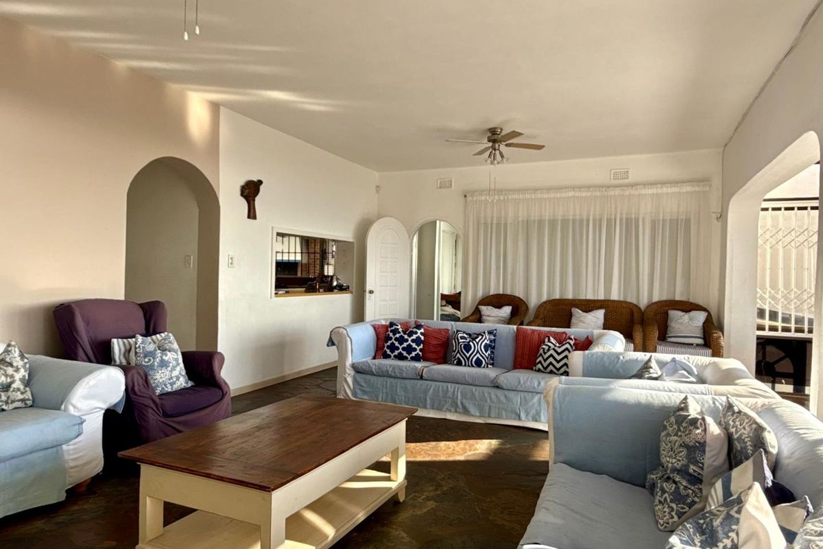 Spacious living room featuring a classic archway, ceiling fan, and large window with natural light, finished with rustic stone-style flooring.