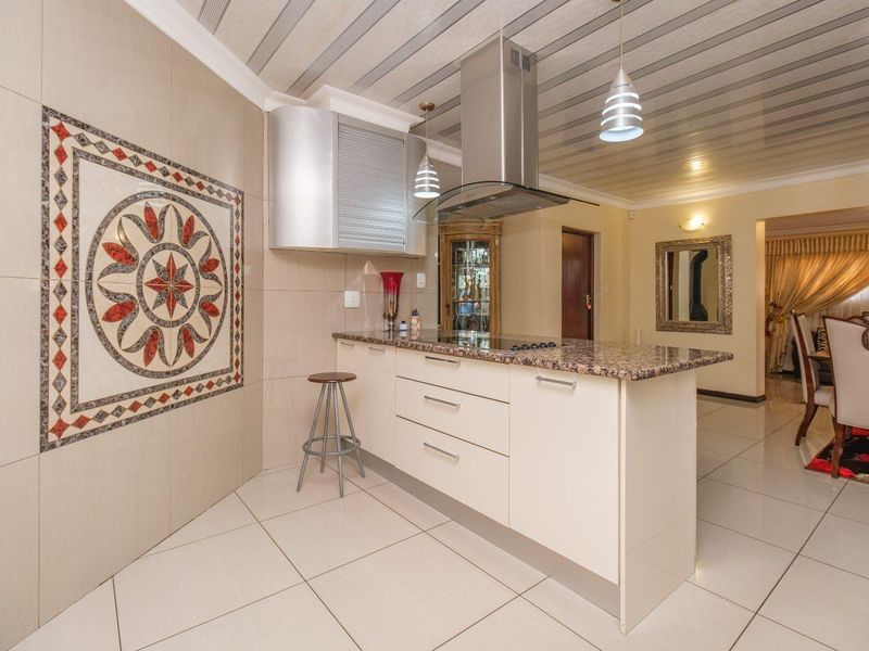 Modern kitchen featuring a granite-topped island, stainless steel extractor fan, and decorative wall tiling, seamlessly flowing into the adjacent dining area.