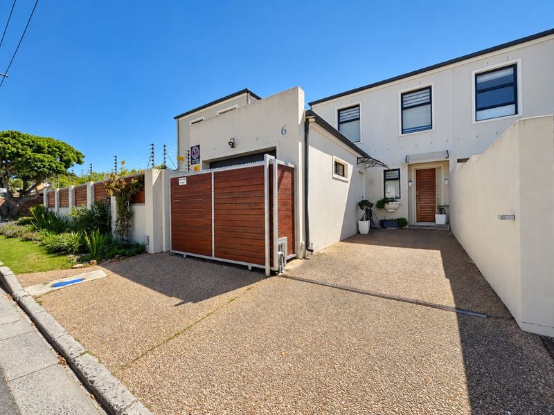 Front elevation of a modern townhouse featuring an exposed aggregate driveway, secure sliding timber gate, and clean rendered facade with aluminium window frames.