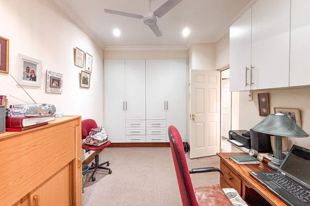 A functional bedroom featuring built-in cupboards, neutral carpeting, and a ceiling fan, currently utilized as a home office space.