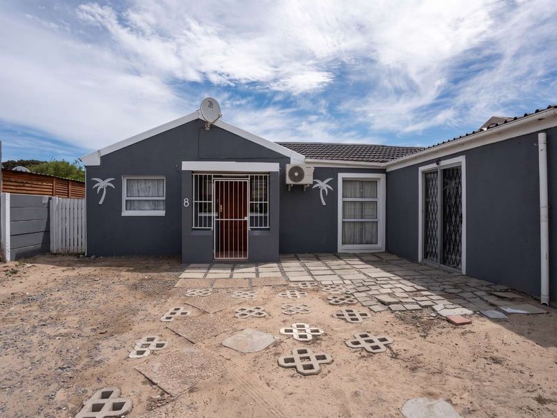 Rear exterior view of a single-story house featuring a paved patio area, security gates, and an external air conditioning unit.