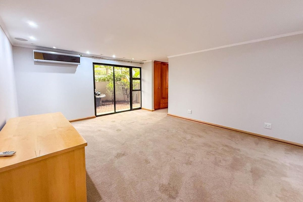 Spacious bedroom featuring neutral carpeting, built-in wooden cabinetry, a wall-mounted air conditioning unit, and sliding glass doors leading to an outdoor area.