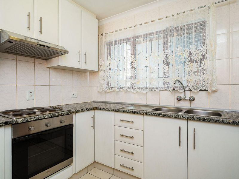 A functional kitchen featuring granite countertops, built-in cabinetry, an electric oven with hob, and a double stainless steel sink with tiled backsplash.