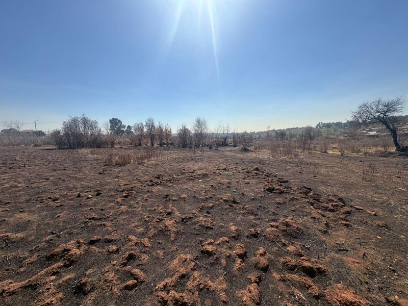 A wide-angle view of a vacant residential plot featuring dry, scorched earth and sparse vegetation under a clear blue sky.