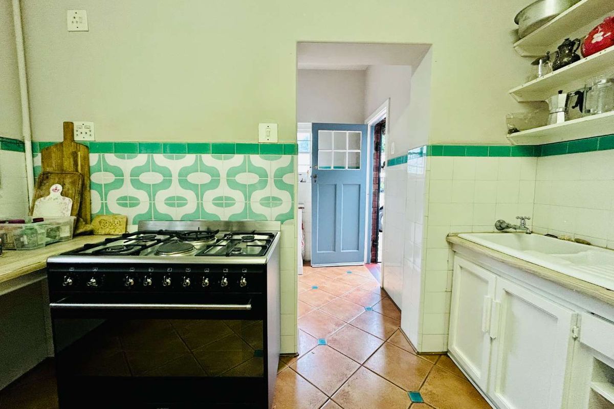 A vintage-style kitchen featuring a freestanding gas stove, tiled backsplash, built-in sink unit, and terracotta floor tiles leading to an exterior doorway.