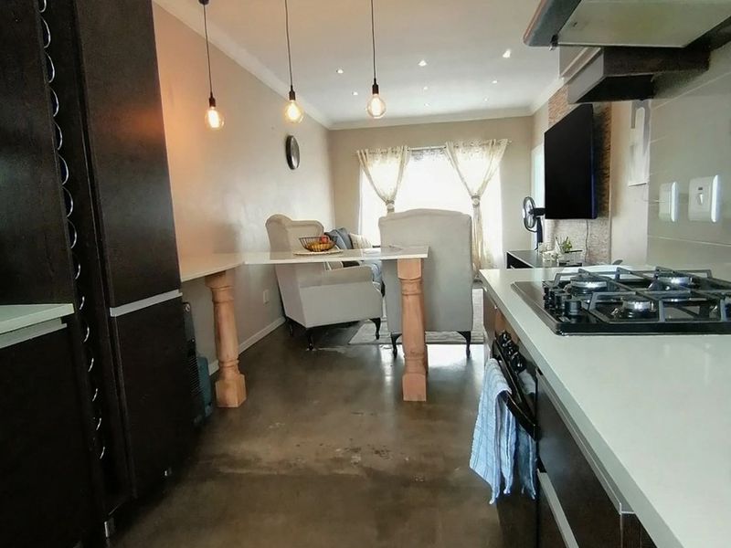 Open-plan kitchen and living area featuring polished concrete floors, modern cabinetry, gas hob, and integrated breakfast bar with pendant lighting.