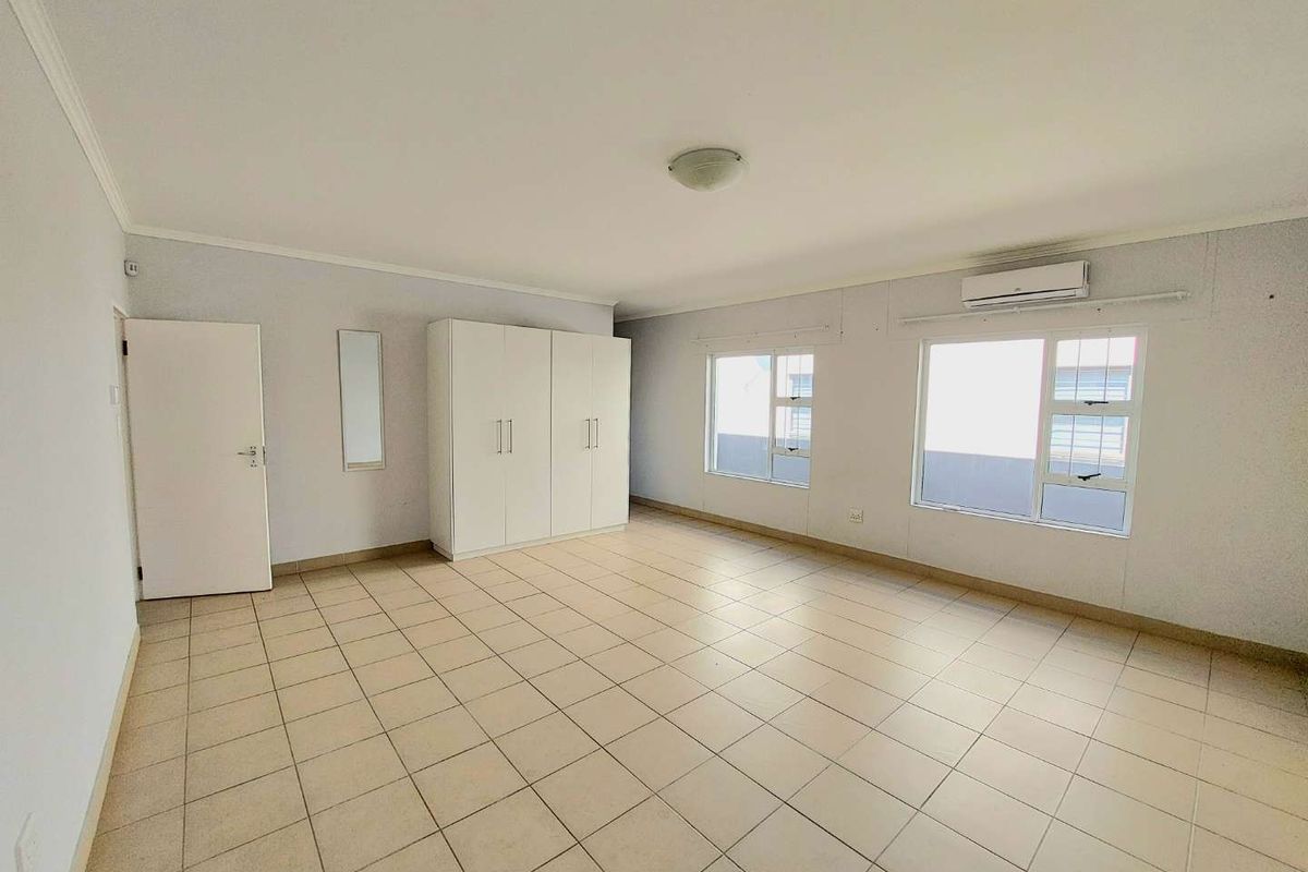 A spacious, light-filled bedroom featuring neutral tiled flooring, built-in cupboards, and a wall-mounted air conditioning unit.