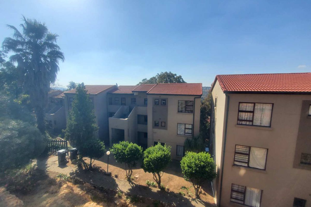 Exterior view of a multi-story apartment complex featuring terracotta tiled roofs and a paved garden walkway area.