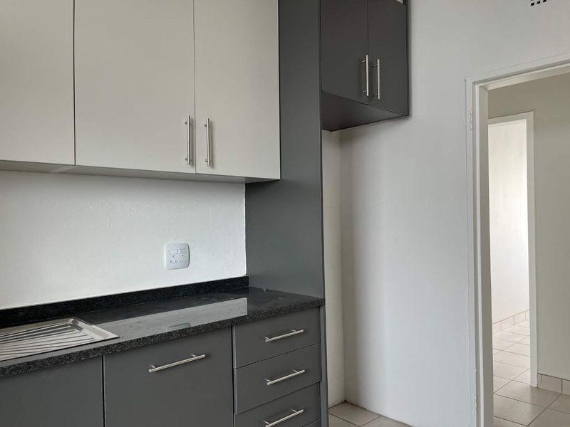 A clean, modern kitchen featuring two-tone cabinetry, granite countertops, and a stainless steel sink, presented in an empty, well-maintained state.