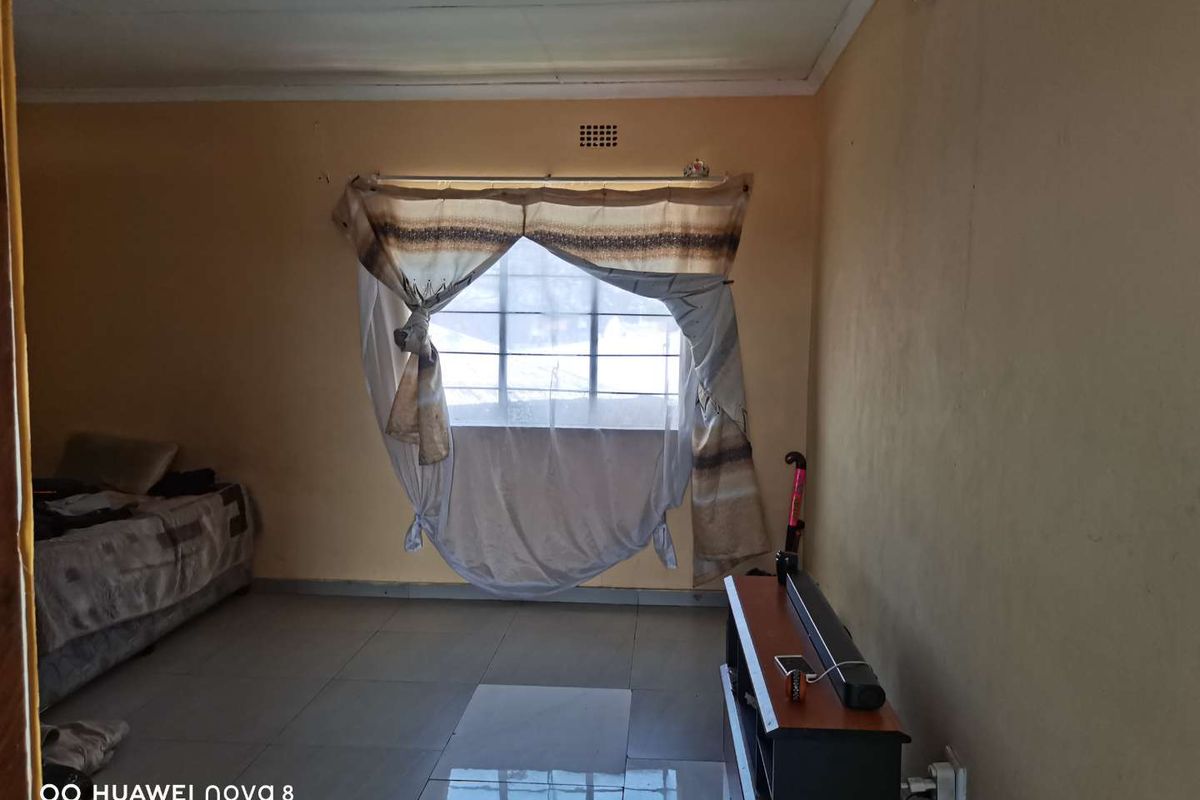 A living room featuring tiled flooring and a window with security bars, requiring cosmetic updates to improve the overall aesthetic and finish.