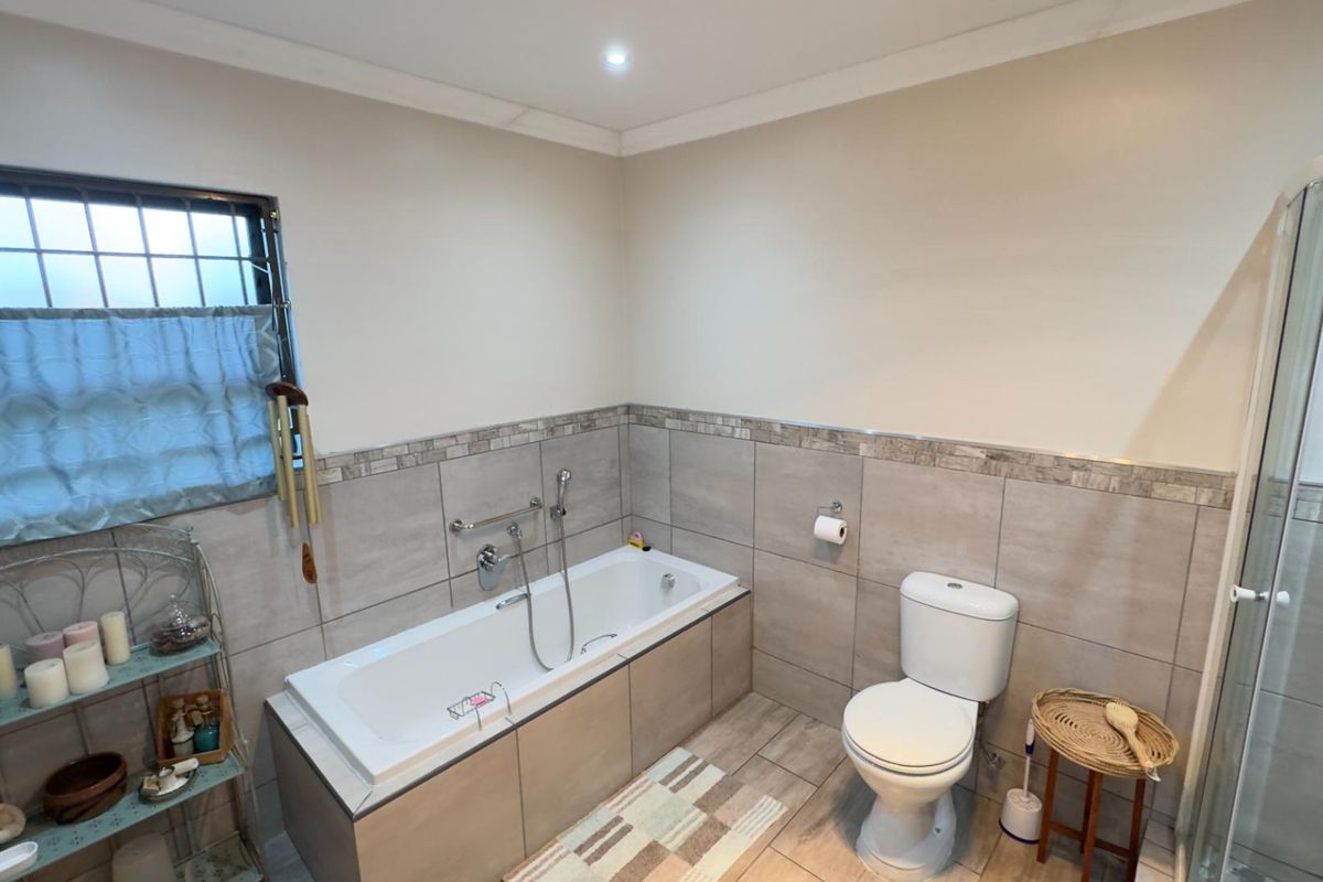 A well-maintained bathroom featuring a built-in bathtub, a modern toilet, and a separate shower enclosure with neutral wall and floor tiling.
