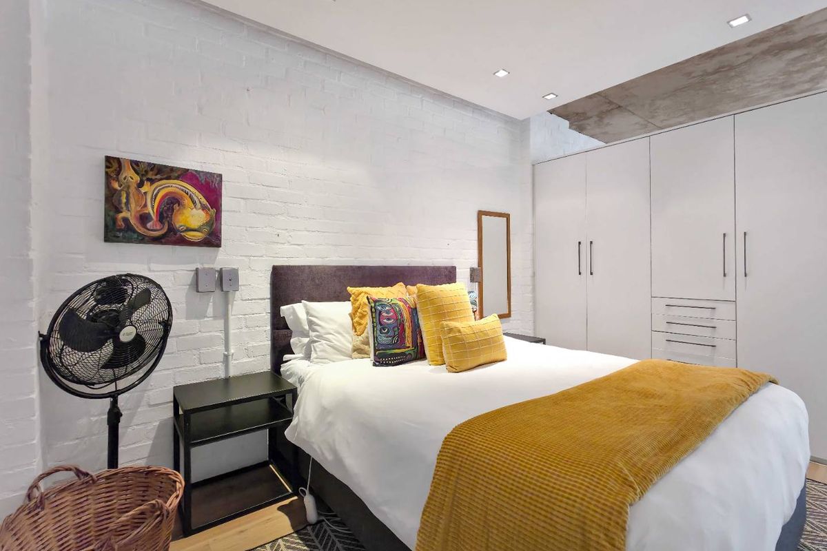 A modern bedroom featuring an exposed brick wall, recessed ceiling lighting, and ample built-in cupboard storage with a contemporary industrial aesthetic.