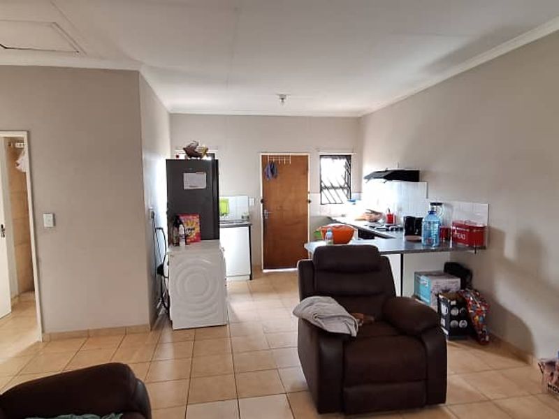 Open-plan living area featuring tiled flooring and a functional kitchen space with built-in cabinetry and a tiled splashback.