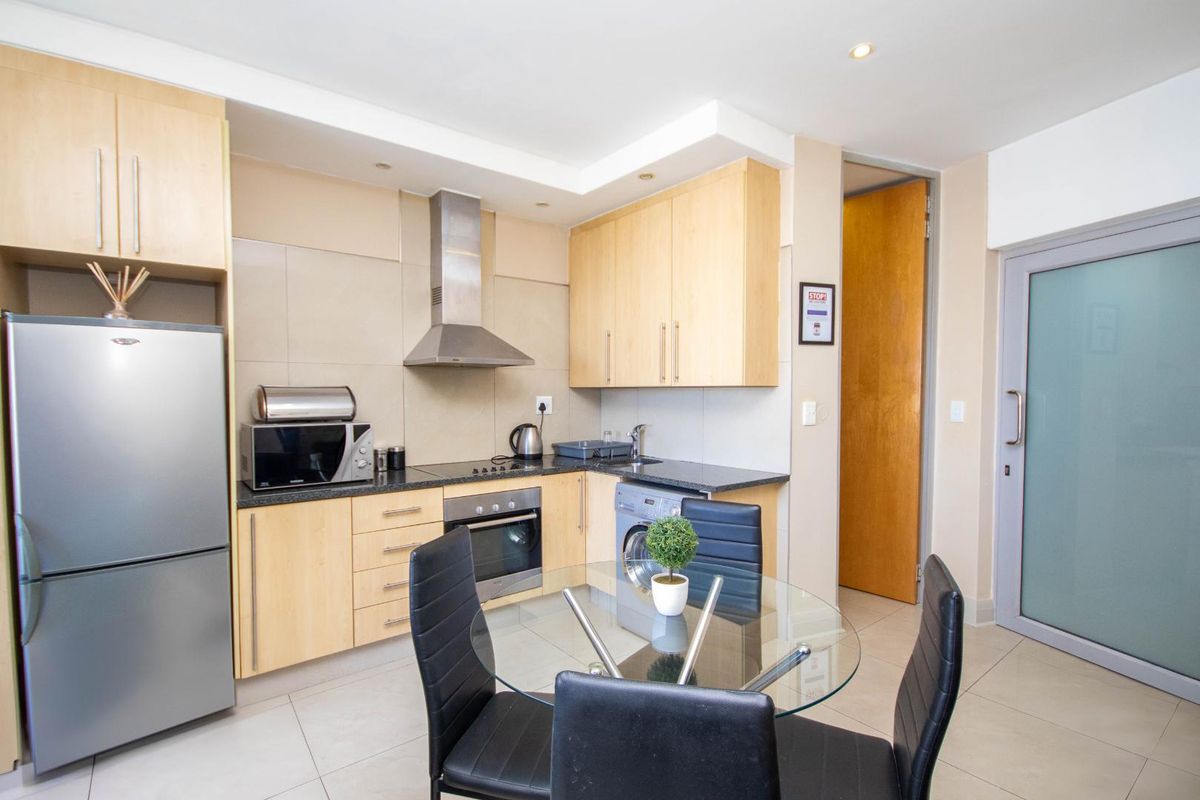 Compact modern kitchen featuring light wood cabinetry, stone countertops, built-in oven, extractor fan, and integrated laundry facilities, finished with neutral floor tiles.