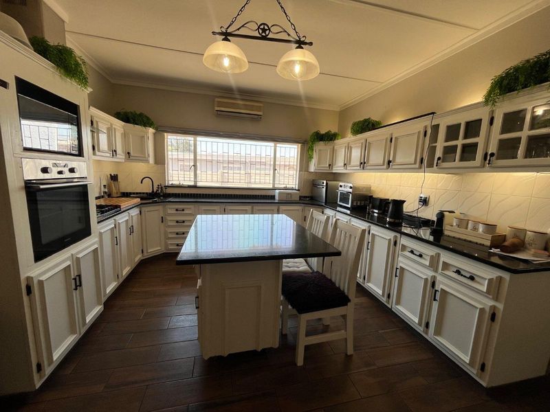 A well-maintained kitchen featuring white cabinetry, dark granite countertops, a central island, built-in appliances, and warm undercabinet lighting.