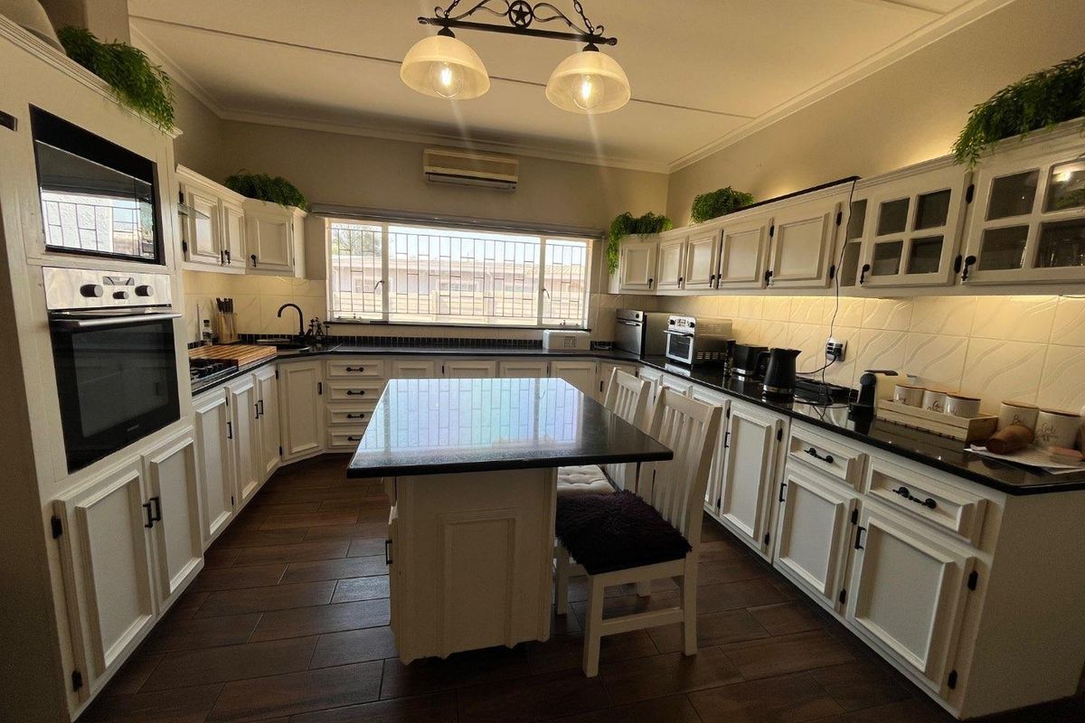 A well-maintained kitchen featuring white cabinetry, dark granite countertops, a central island, built-in appliances, and warm undercabinet lighting.