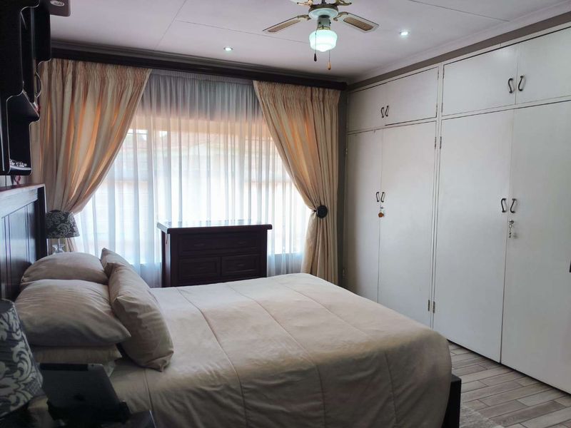 A bedroom featuring built-in cupboards, tiled flooring, and a ceiling fan, offering a functional space with neutral finishes.