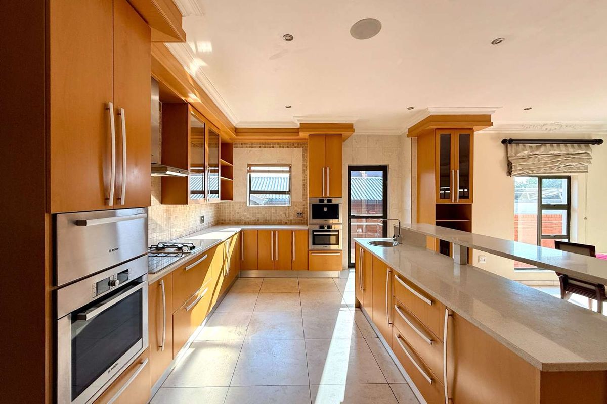 Spacious kitchen featuring warm wood cabinetry, stone countertops, integrated appliances, and a large breakfast bar island with tiled flooring.