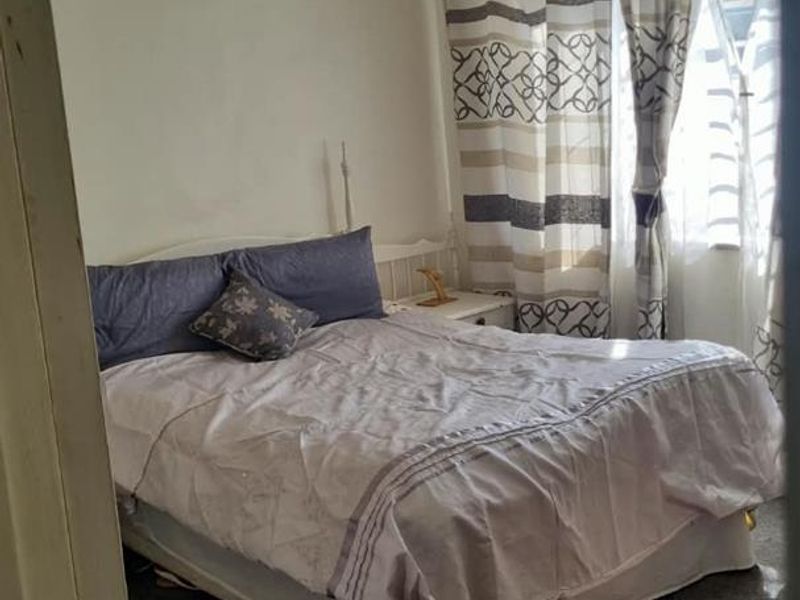 A bedroom featuring louvered windows and ceiling tiles, currently showing signs of wear on the carpet and walls.