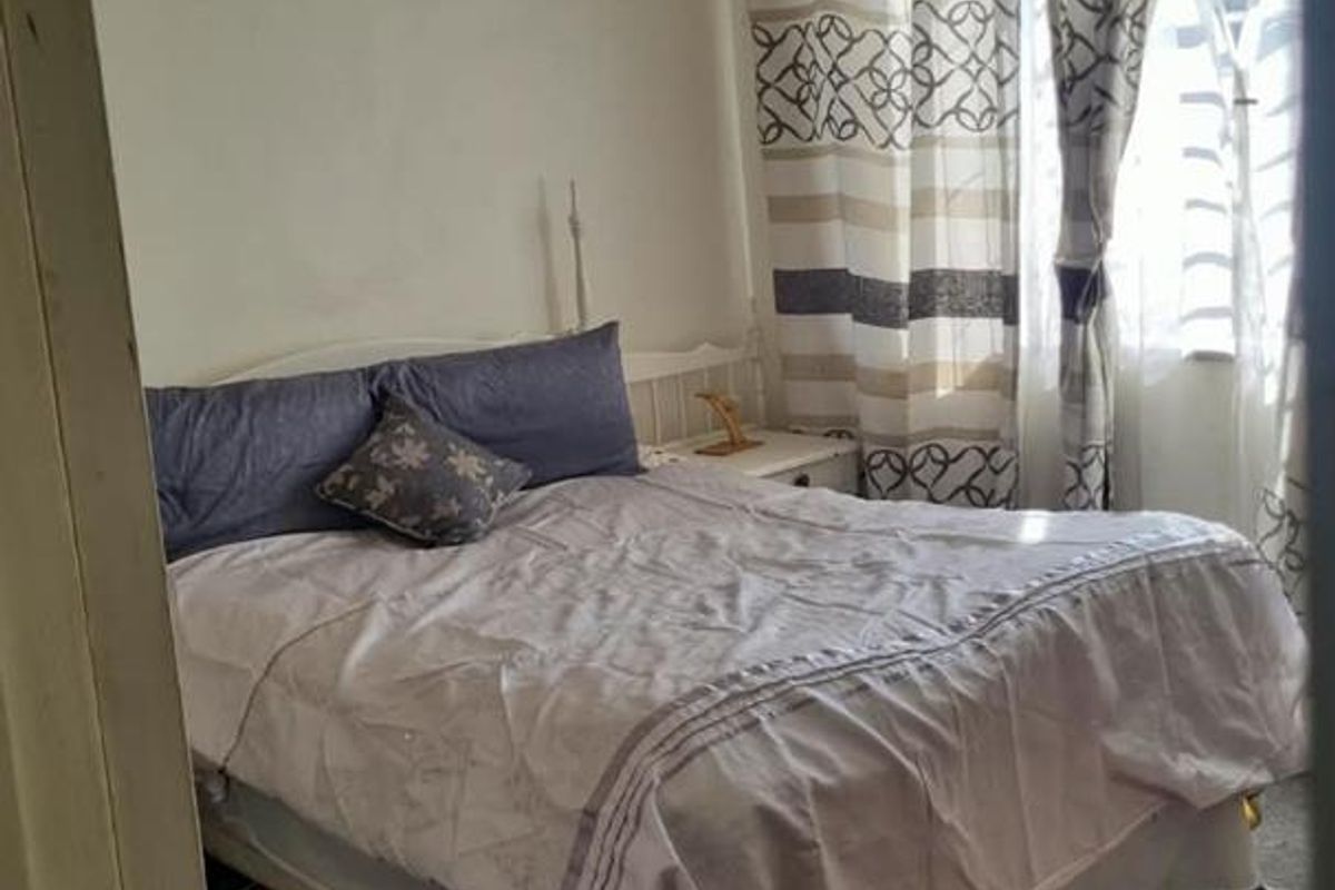 A bedroom featuring louvered windows and ceiling tiles, currently showing signs of wear on the carpet and walls.