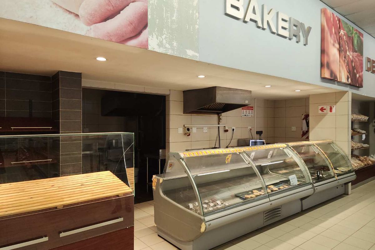 Commercial bakery section featuring built-in refrigerated display counters, tiled flooring, recessed lighting, and integrated ventilation hood.