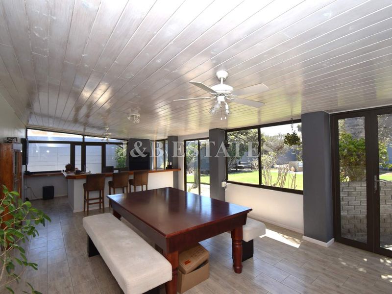 Spacious open-plan entertainment area featuring a built-in bar, tiled flooring, wood-paneled ceiling, and large windows overlooking the garden.